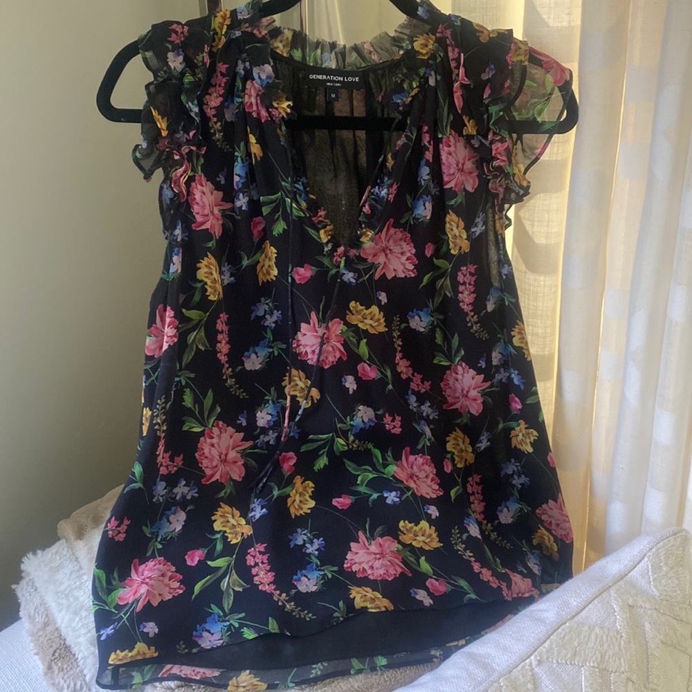 Black floral sleeveless shirt with ruffle sleeve and tie neck.